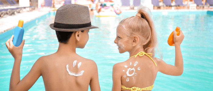Kids practicing sun safety for kids by applying sunscreen sitting by the pool